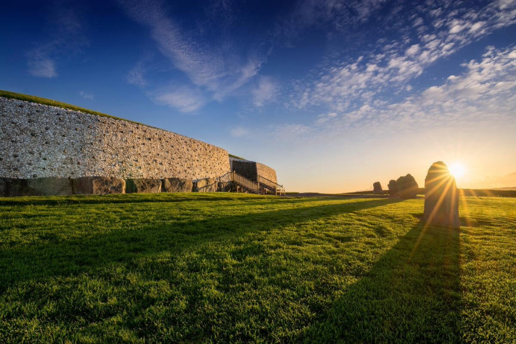 The ancient passage tomb of Newgrange in County Meath, with its white quartz stone facade and standing stones at sunset.