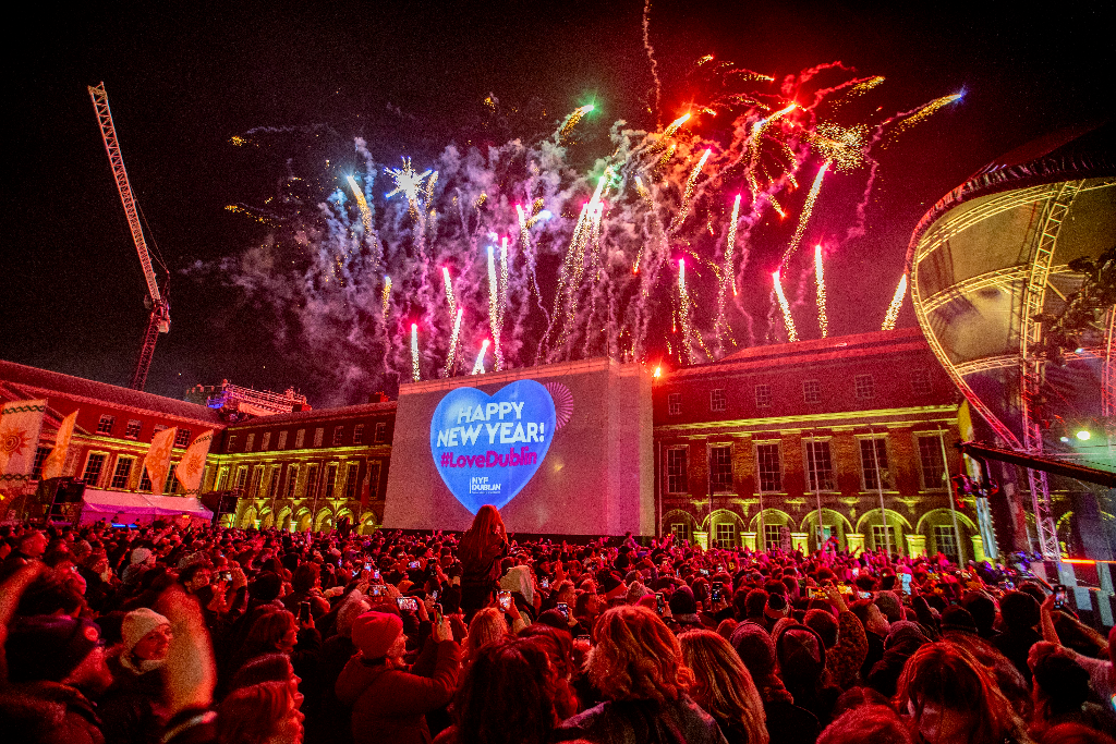 Colourful fireworks lighting up the night sky above Dublin Castle during New Year's Festival Dublin, with a large crowd watching and a Happy New Year projection on the building.
