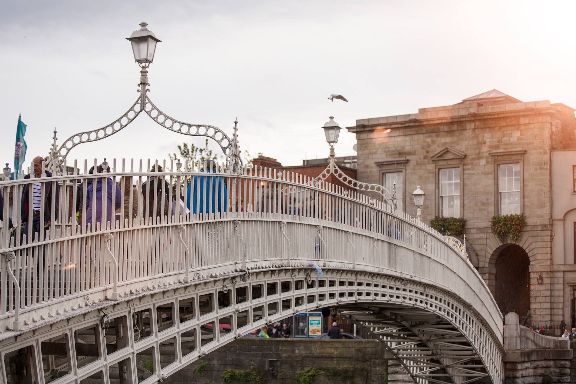 People crossing the white cast-iron Ha’penny Bridge over the River Liffey in Dublin city centre.
