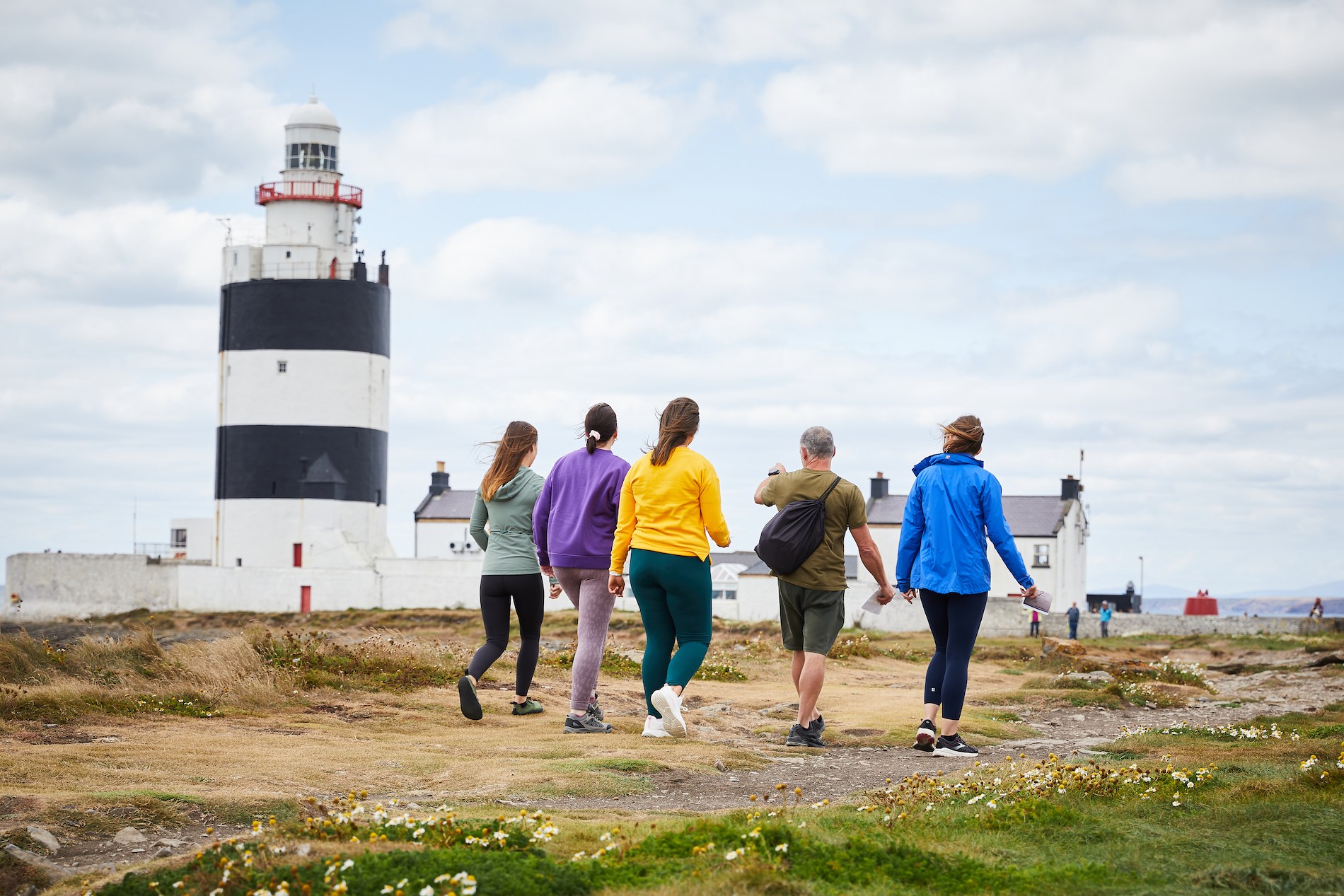 Visitors walking along the coast towards Hook Lighthouse, County Wexford, Ireland’s oldest operational lighthouse.