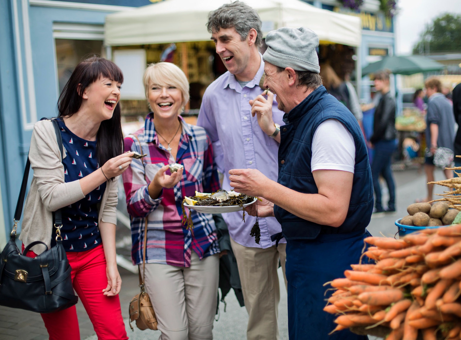Group enjoying fresh seafood at an outdoor market stall in Galway, with carrots and produce nearby.