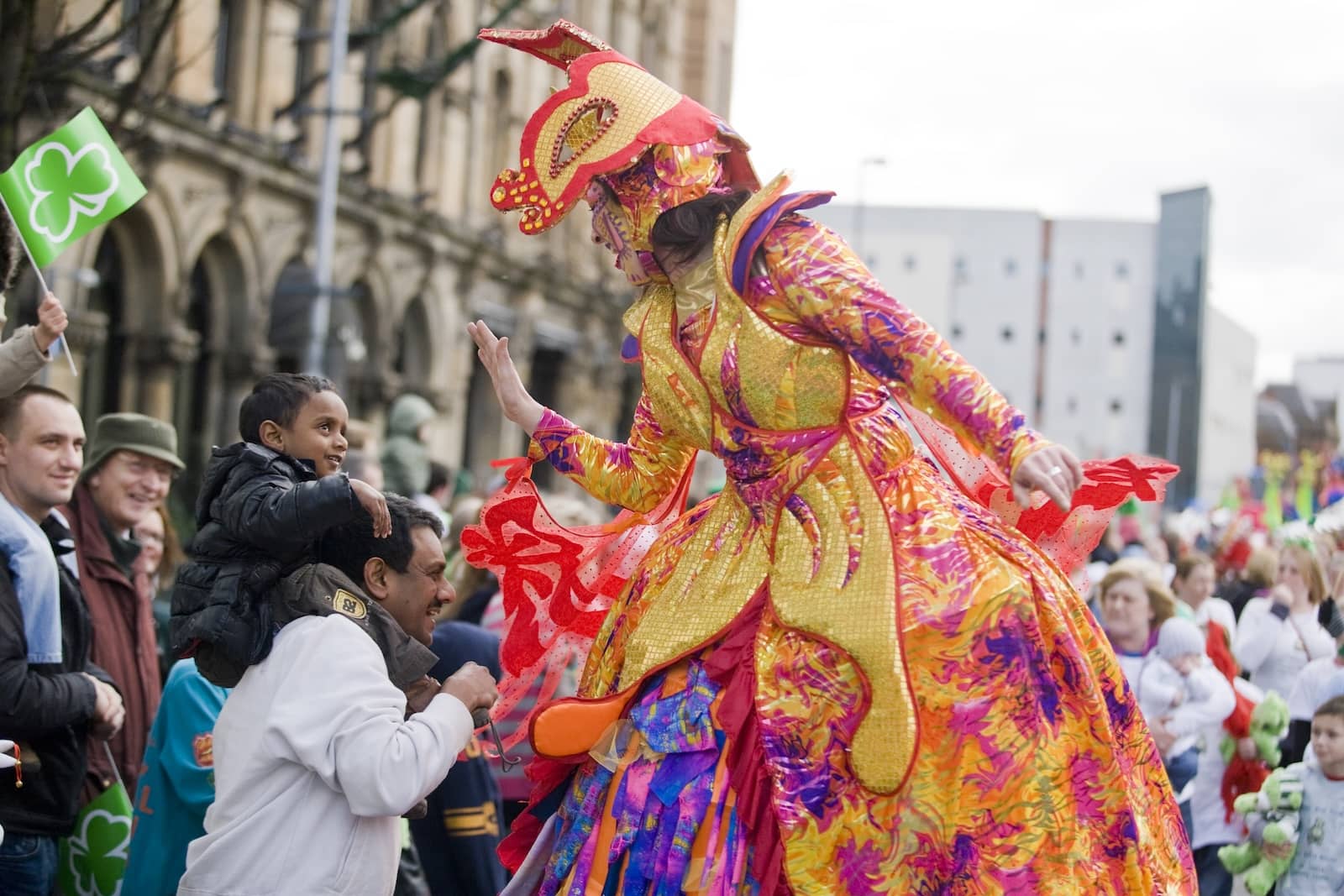 Performer in vibrant costume high-fives a child during Belfast’s St Patrick’s Day parade.