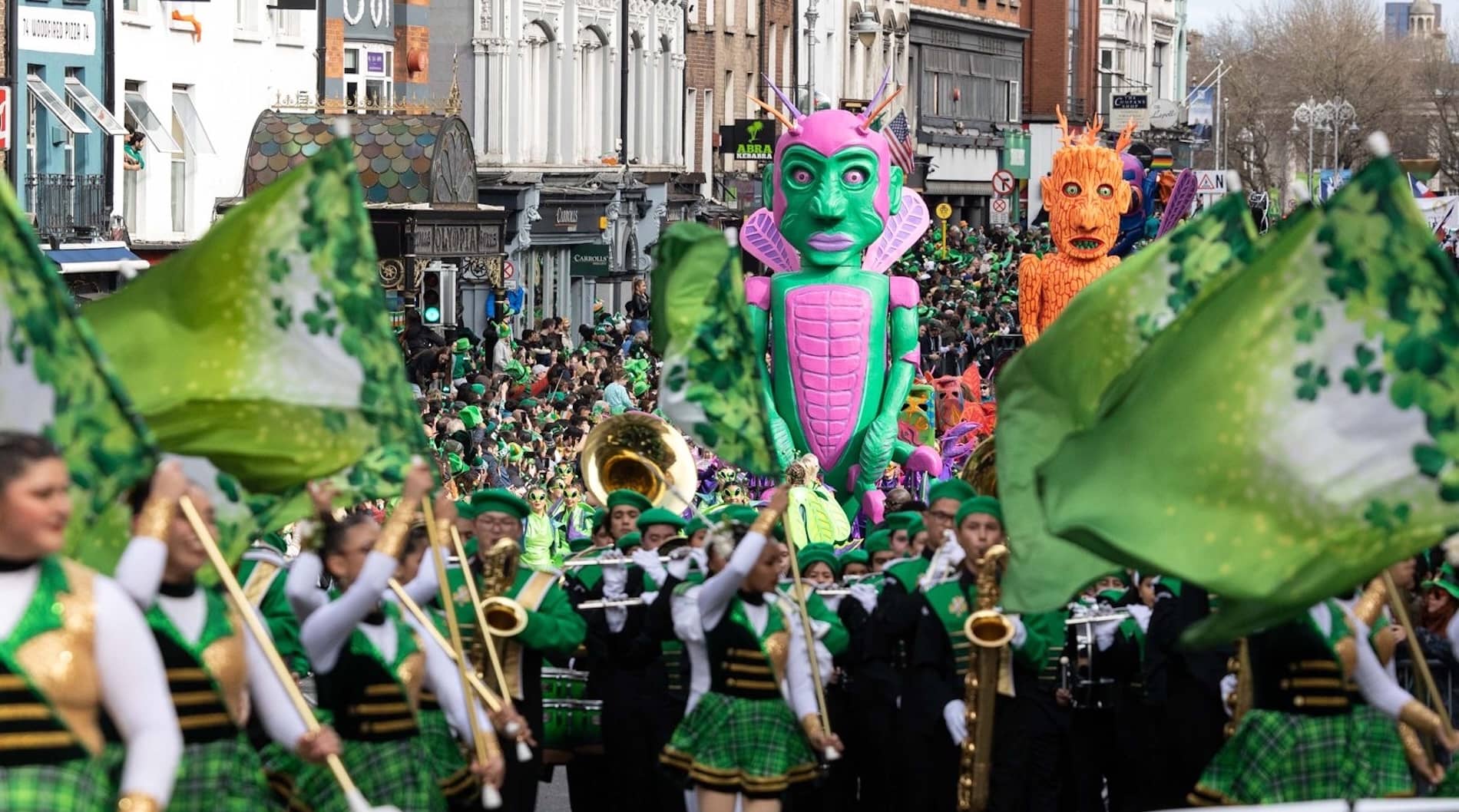Marching band with green flags and giant fantasy figures at Dublin’s St Patrick’s Day parade.