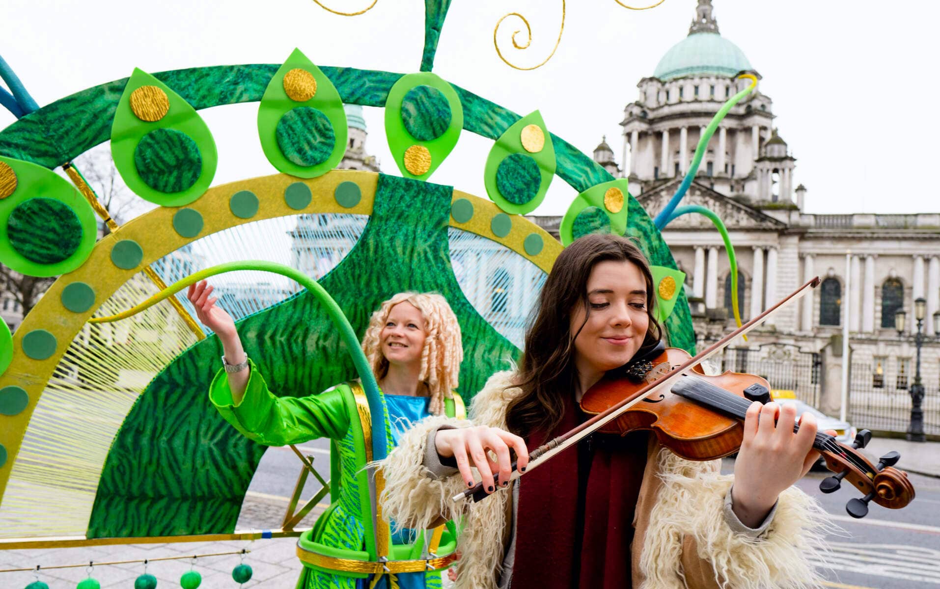 Un musicien joue du violon à côté d'un artiste en vert lors d'un défilé de la Saint Patrick à l'extérieur de l'hôtel de ville de Belfast.