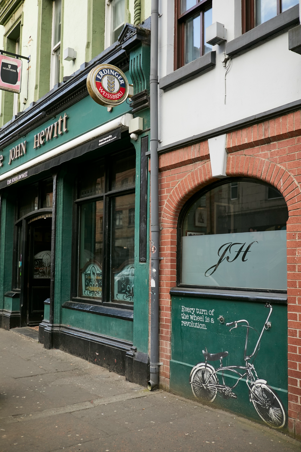 The John Hewitt pub in Belfast, with its traditional green frontage and bicycle artwork on the exterior wall.