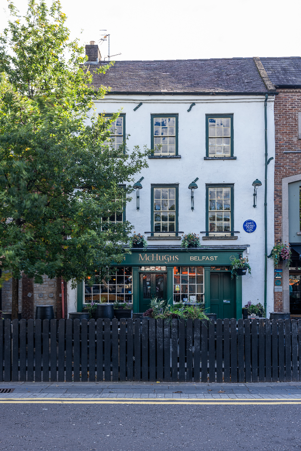 McHugh’s Bar in Belfast, a traditional white-fronted pub with green trim and hanging flower baskets.