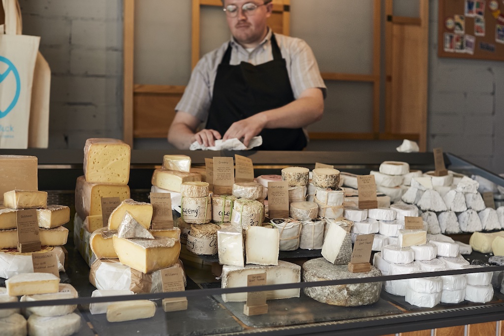 A cheesemonger with an array of different cheeses on display in the Cathedral Quarter, Belfast.