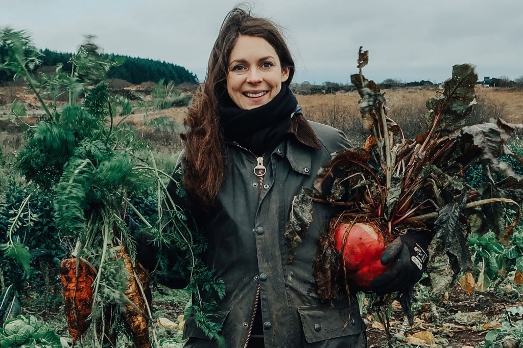 Donna sorridente che tiene carote e barbabietole appena raccolte nella fattoria di Broughgammon, nella contea di Antrim.