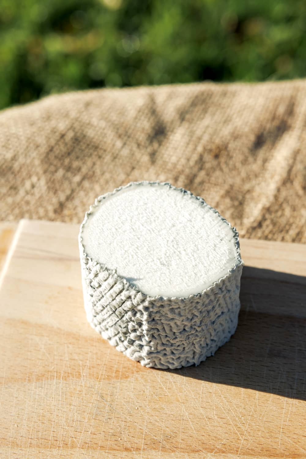 A round wheel of St Tola goat cheese resting on a wooden board outdoors.