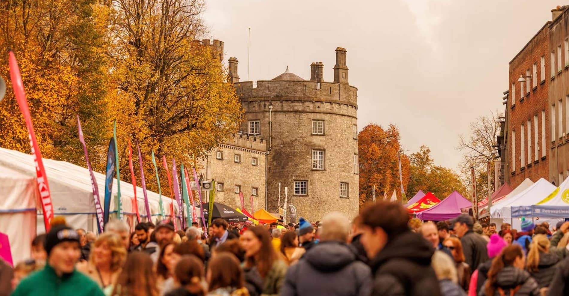 Crowds browse colourful food stalls outside Kilkenny Castle during the Savour Kilkenny Food Festival in autumn.