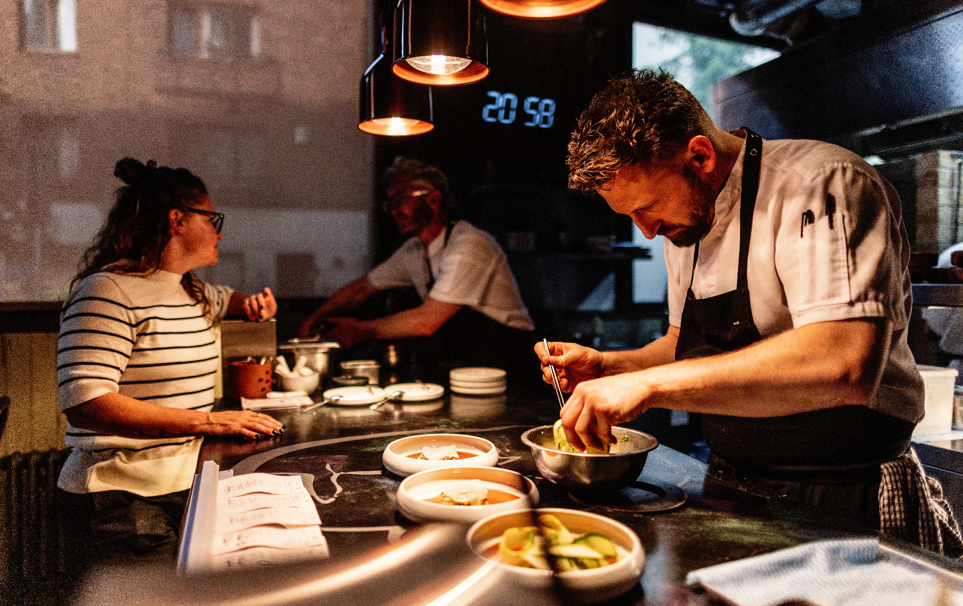 A chef carefully prepares and plates dishes in the warmly lit open kitchen at Variety Jones in Dublin.