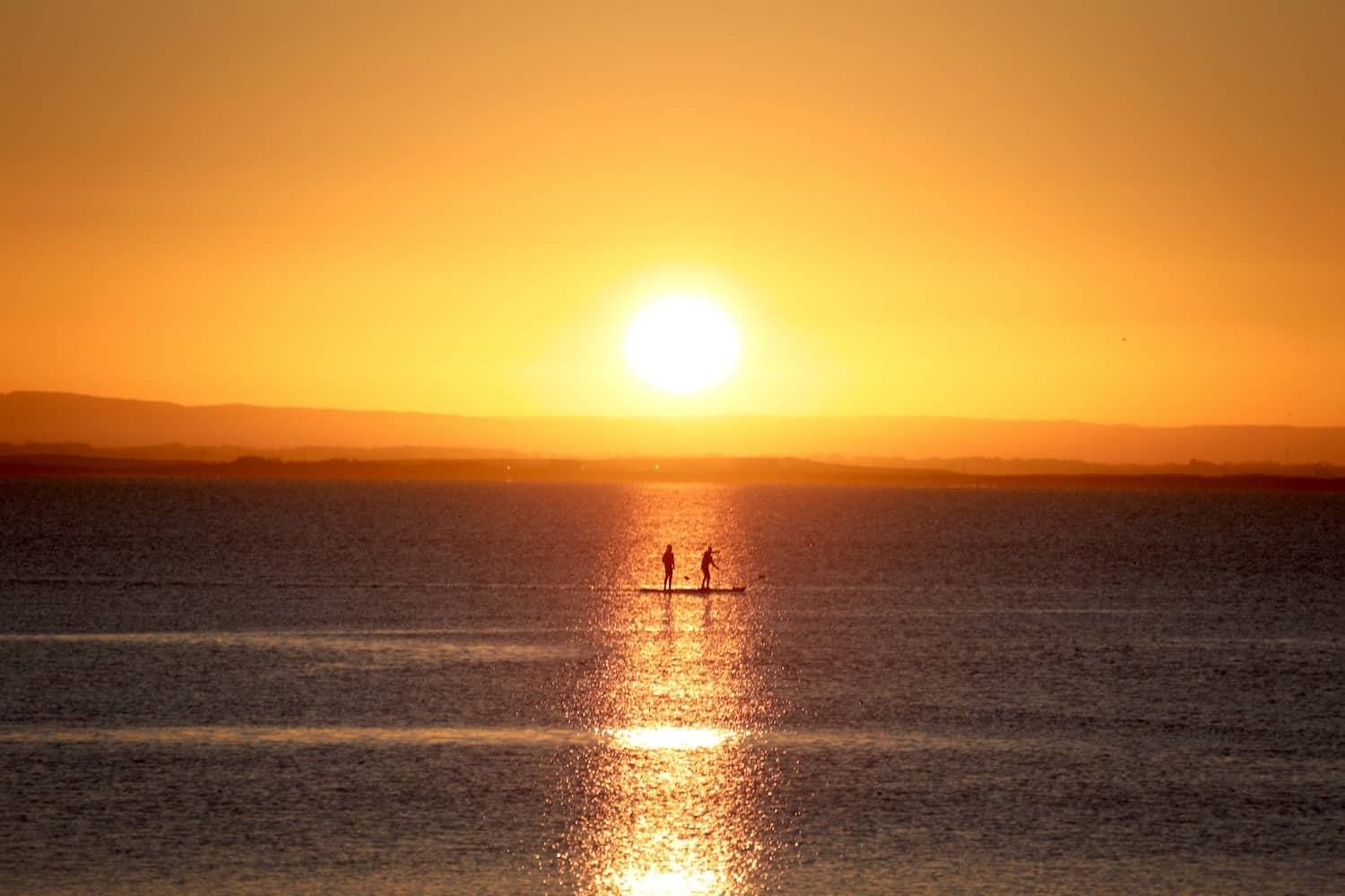 Paddleboarders silhouetted against the sunset on Galway Bay in Salthill, Galway.