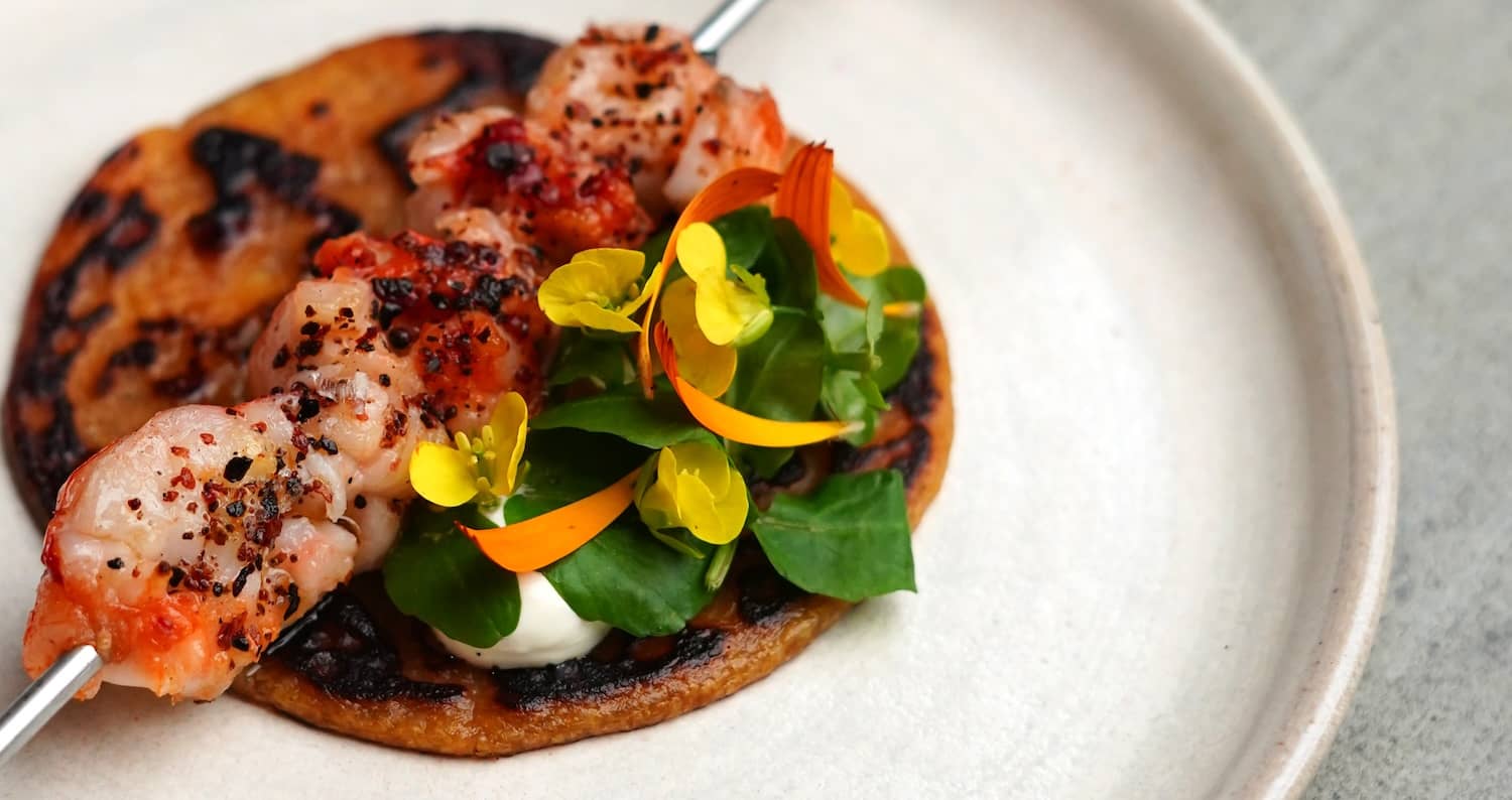 Gegrillte Garnelen mit essbaren Blüten und frischem Grün auf einem angeschwärzten Fladenbrot serviert im Dede, Grafschaft Cork.