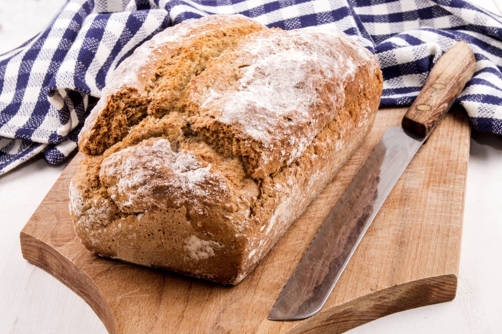 Traditional Irish brown soda bread on a wooden board with serrated knife.