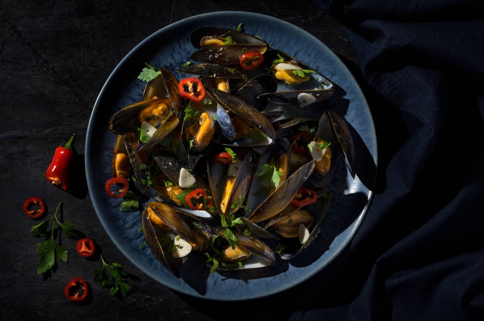 Steamed mussels in a dark bowl with chilli, garlic and fresh herbs.
