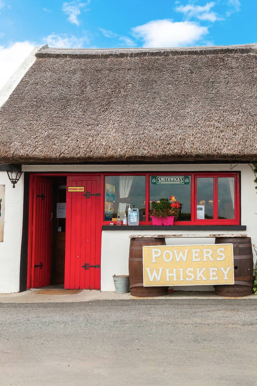Een pub met een traditioneel rieten dak, felrode deuren en een Powers whiskey-reclamebord in Sligo.