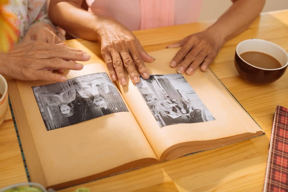 Hands looking through an old photo album with black-and-white family pictures on a wooden table.