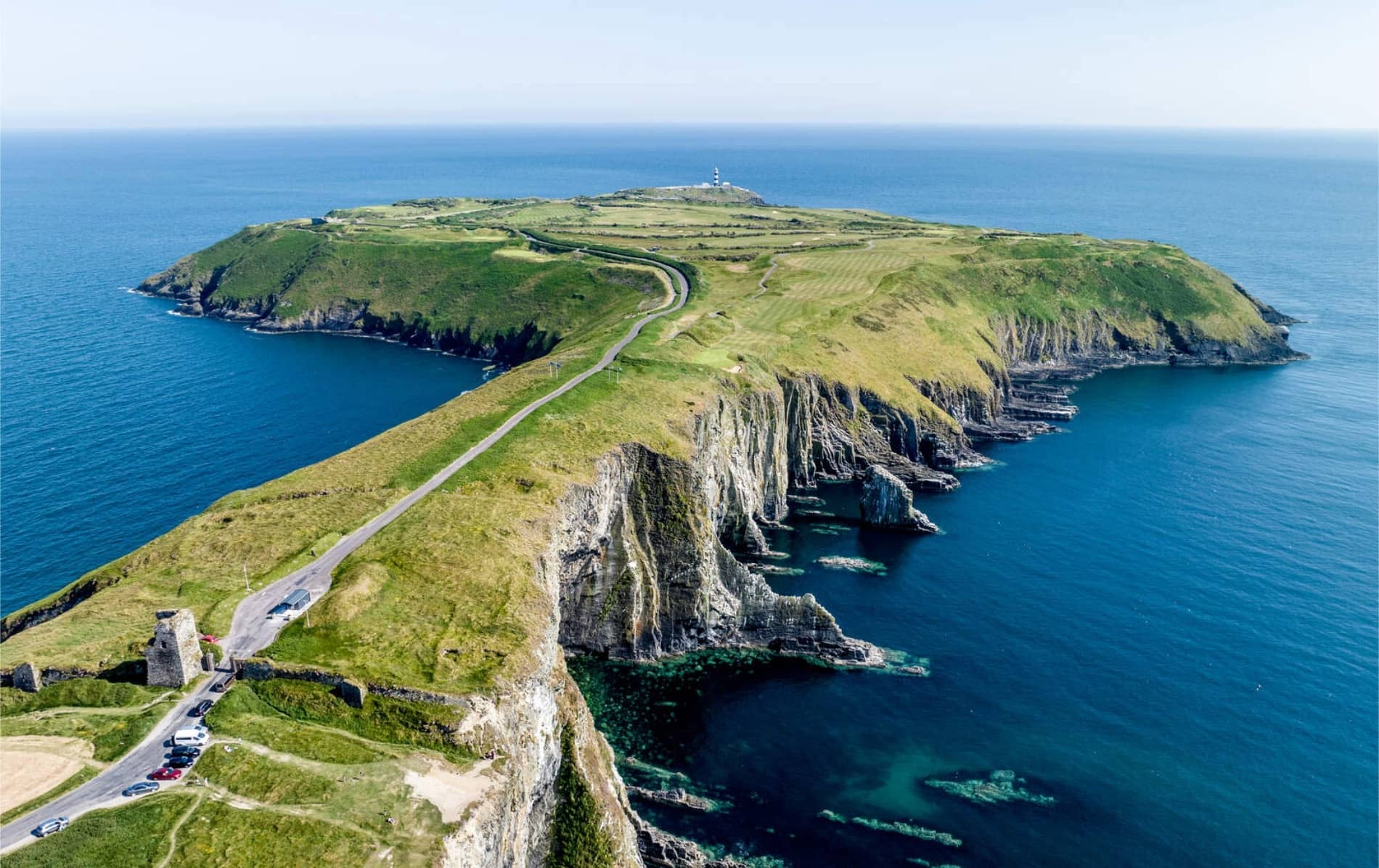 Aerial view of Old Head of Kinsale, showing dramatic sea cliffs, winding road, and lighthouse at the peninsula’s tip.