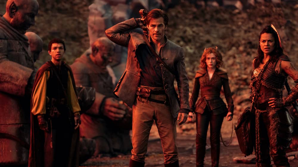 Besetzung von Dungeons & Dragons: Honor Among Thieves im Kostüm, stehend zwischen riesigen Steinstatuen in einer Fantasy-Szene.