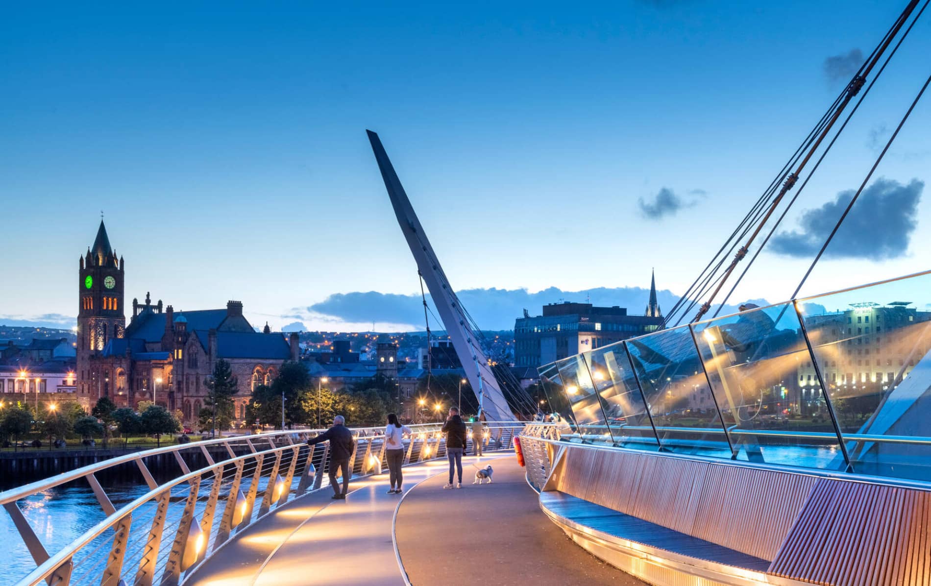 Evening view of the Peace Bridge in Derry~Londonderry, with Guildhall and city skyline lit against the sky.