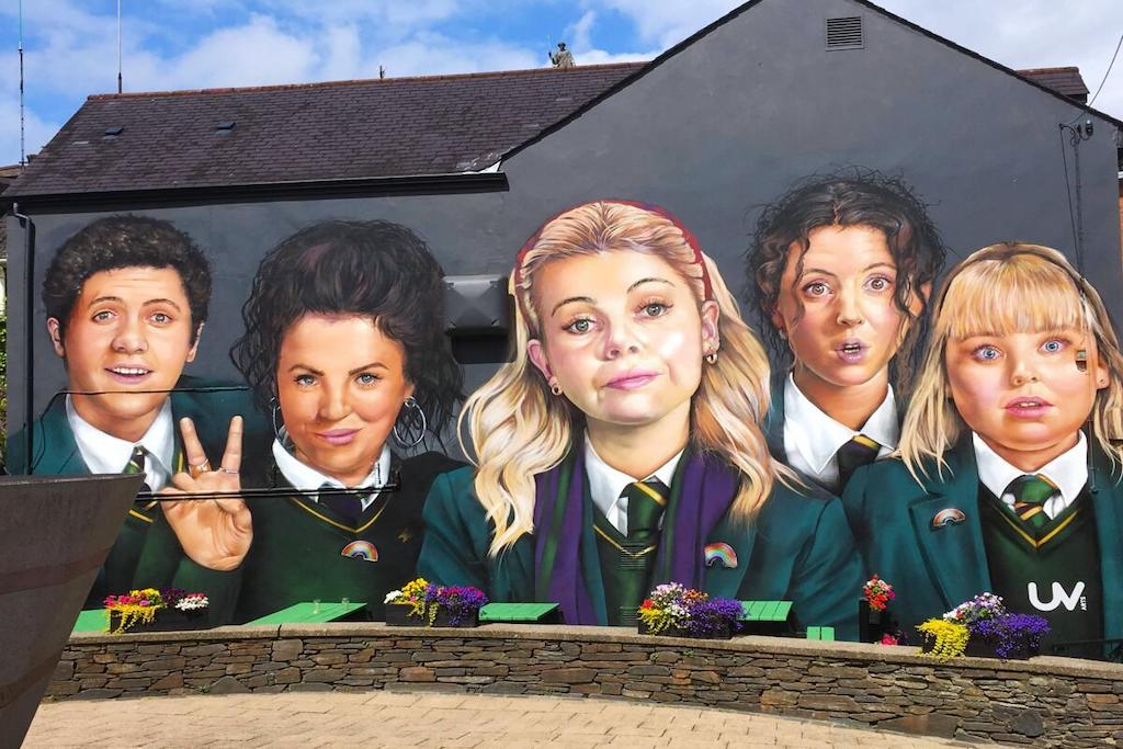 Colourful mural of five school pupils in Derry Girls, wearing uniforms and smiling in Derry~Londonderry.