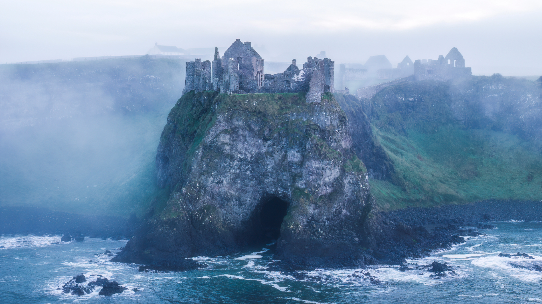 Ruined Dunluce Castle above the Atlantic Ocean in misty weather on the County Antrim coast.