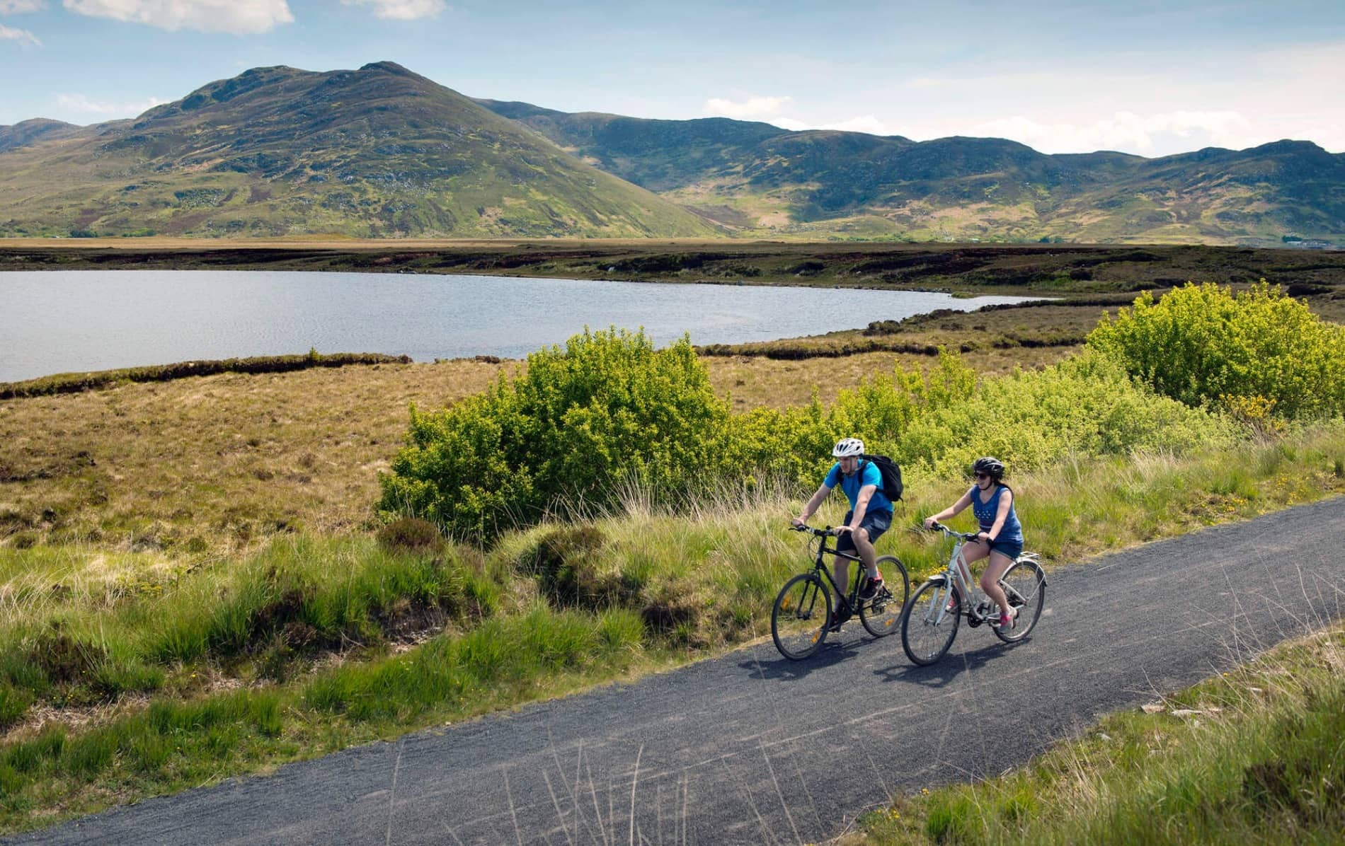 Two cyclists riding along the Great Western Greenway with mountains and a lake in the background, County Mayo.