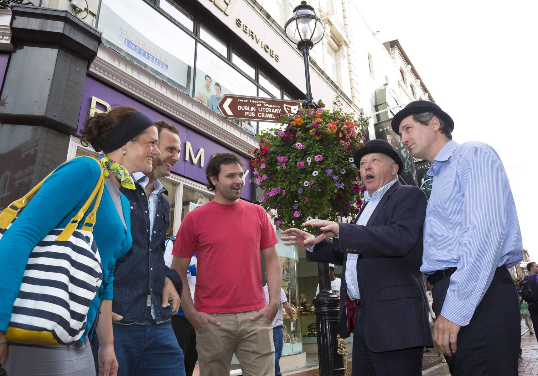 Tour guide speaks to a group outside a Dublin bar on a Dublin Literary Pub Crawl tour near a hanging flower basket.