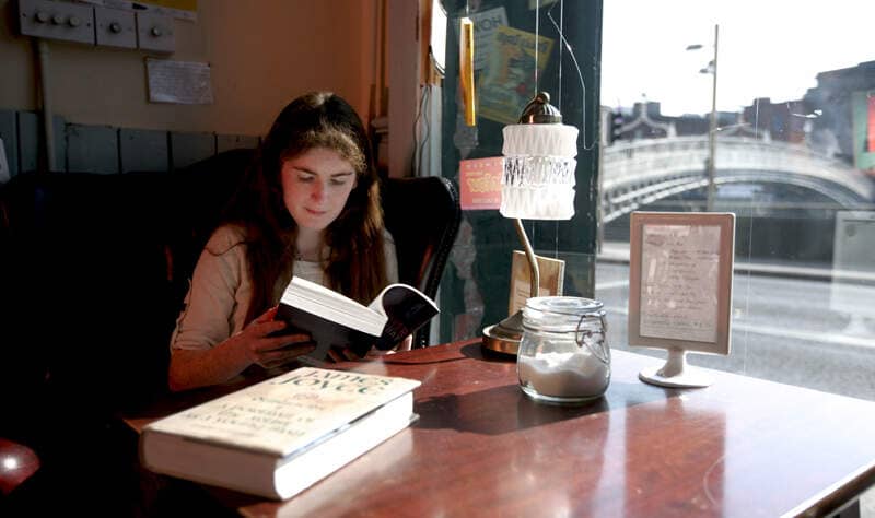 Person reading a book in a Dublin café by a window overlooking the Ha'penny Bridge and the River Liffey.