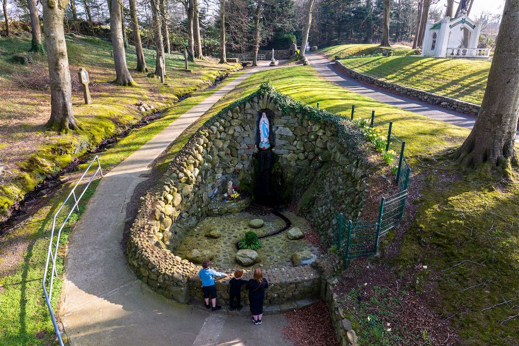 Children standing at St Brigid’s holy well in Faughart, Louth, a stone shrine with statue and natural spring set in woodland.