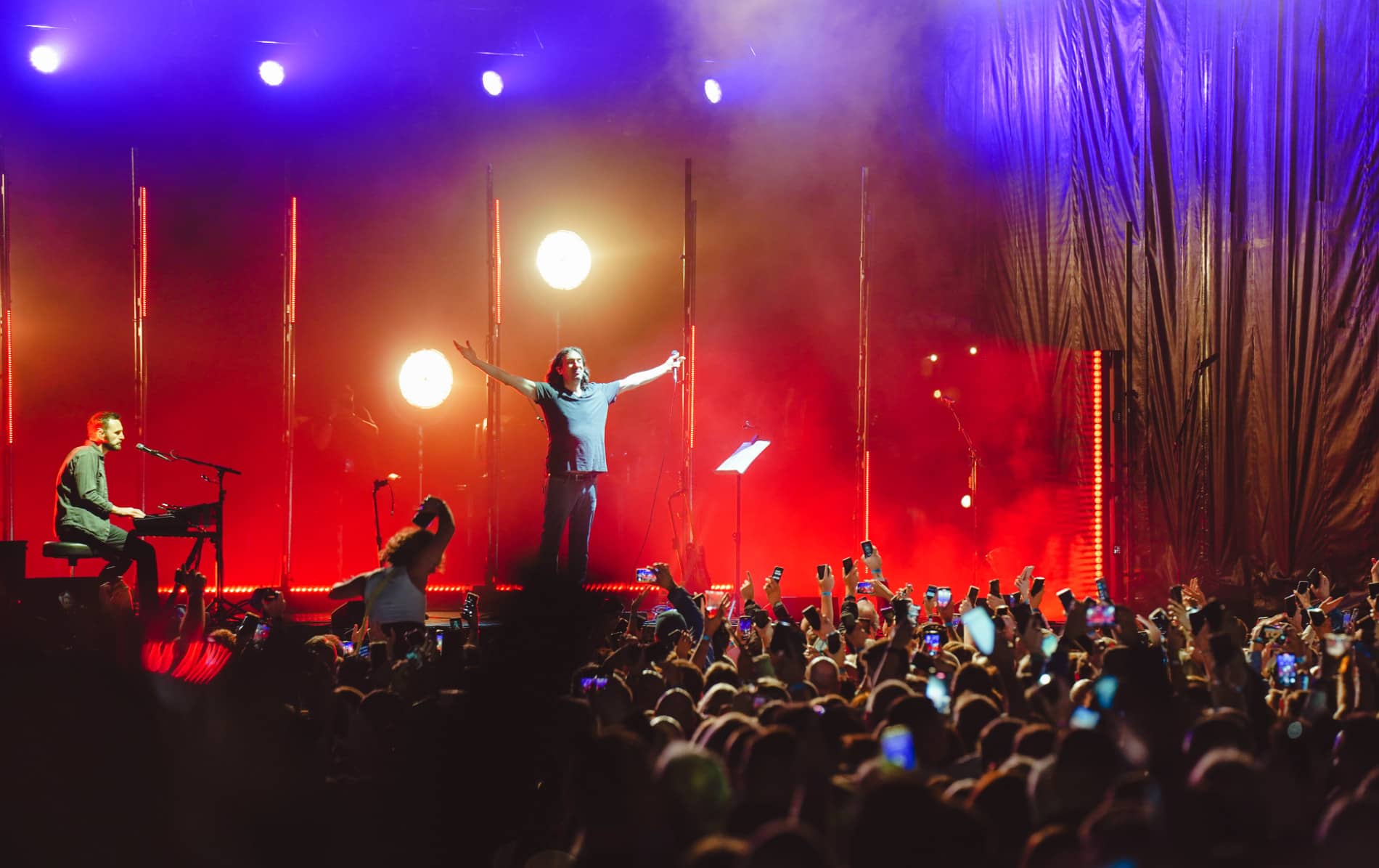 De leadzanger van Snow Patrol zingt met zijn armen wijd uitgestoken voor een juichende menigte en rood-oranje podiumverlichting.