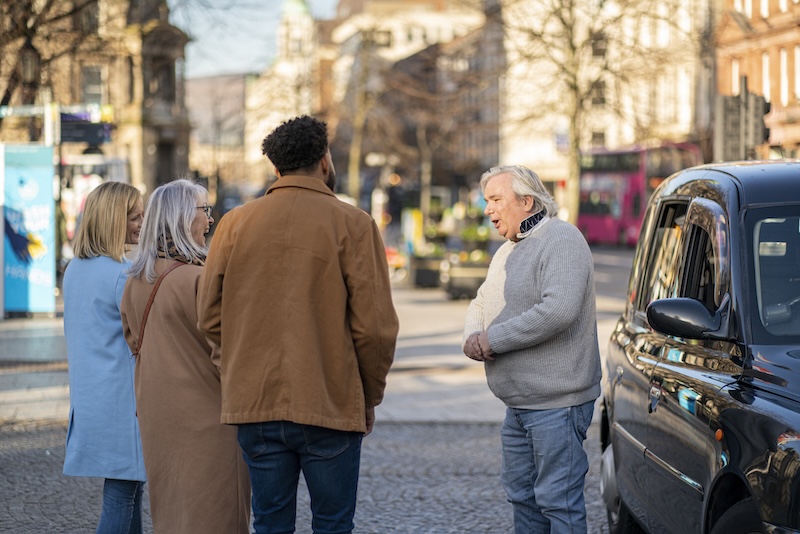 Una guida locale parla con i visitatori durante un Black Taxi Tour in una via di Belfast.