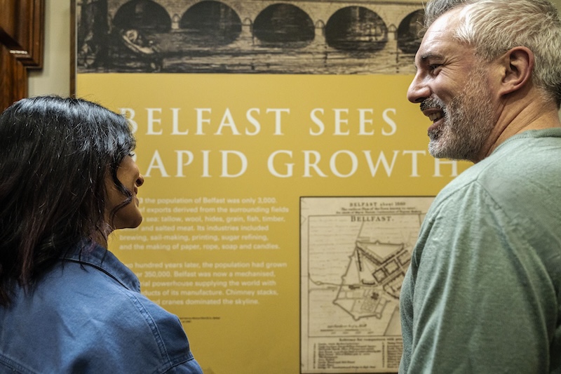 Due visitatori leggono un pannello espositivo sull'espansione di Belfast all'interno della City Hall.