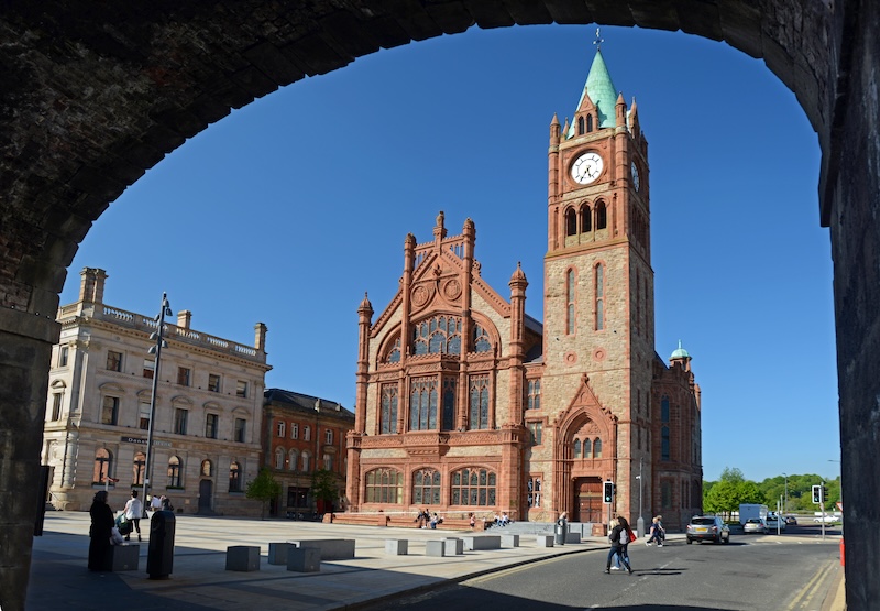 La Guildhall di Derry~Londonderry con la sua torre dell'orologio, incorniciata da edifici storici, in una giornata di sole.