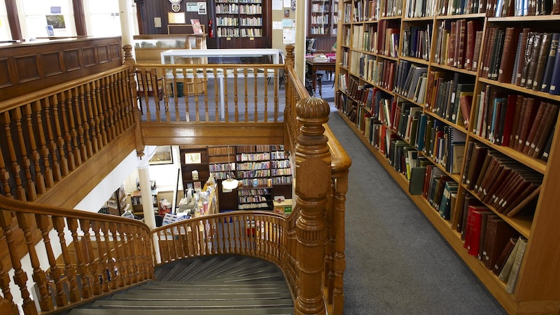 Veduta di una scala in legno che porta alla storica Linen Hall Library di Belfast, con scaffali pieni di libri antichi.