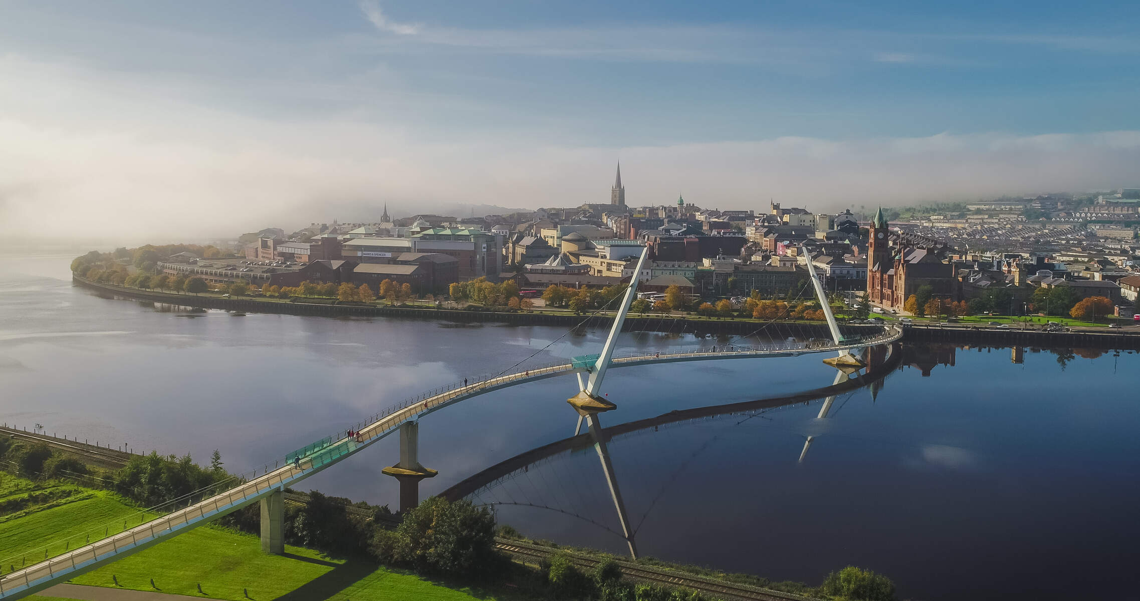 Aerial view of a bridge curving over a wide river towards a city skyline.