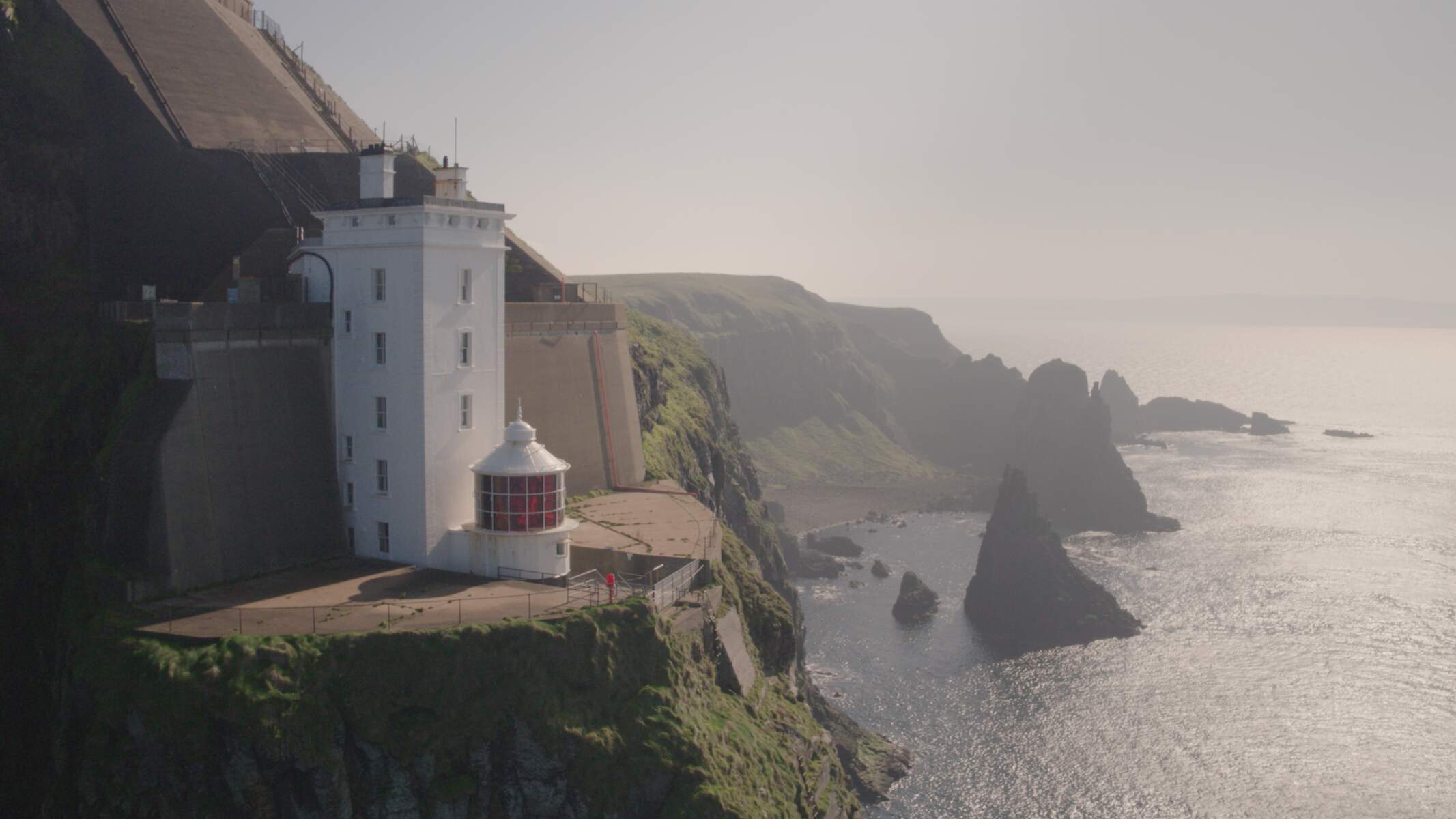White lighthouse perched on a cliff edge at Rathlin Island with dramatic sea stacks rising from the misty Atlantic below.