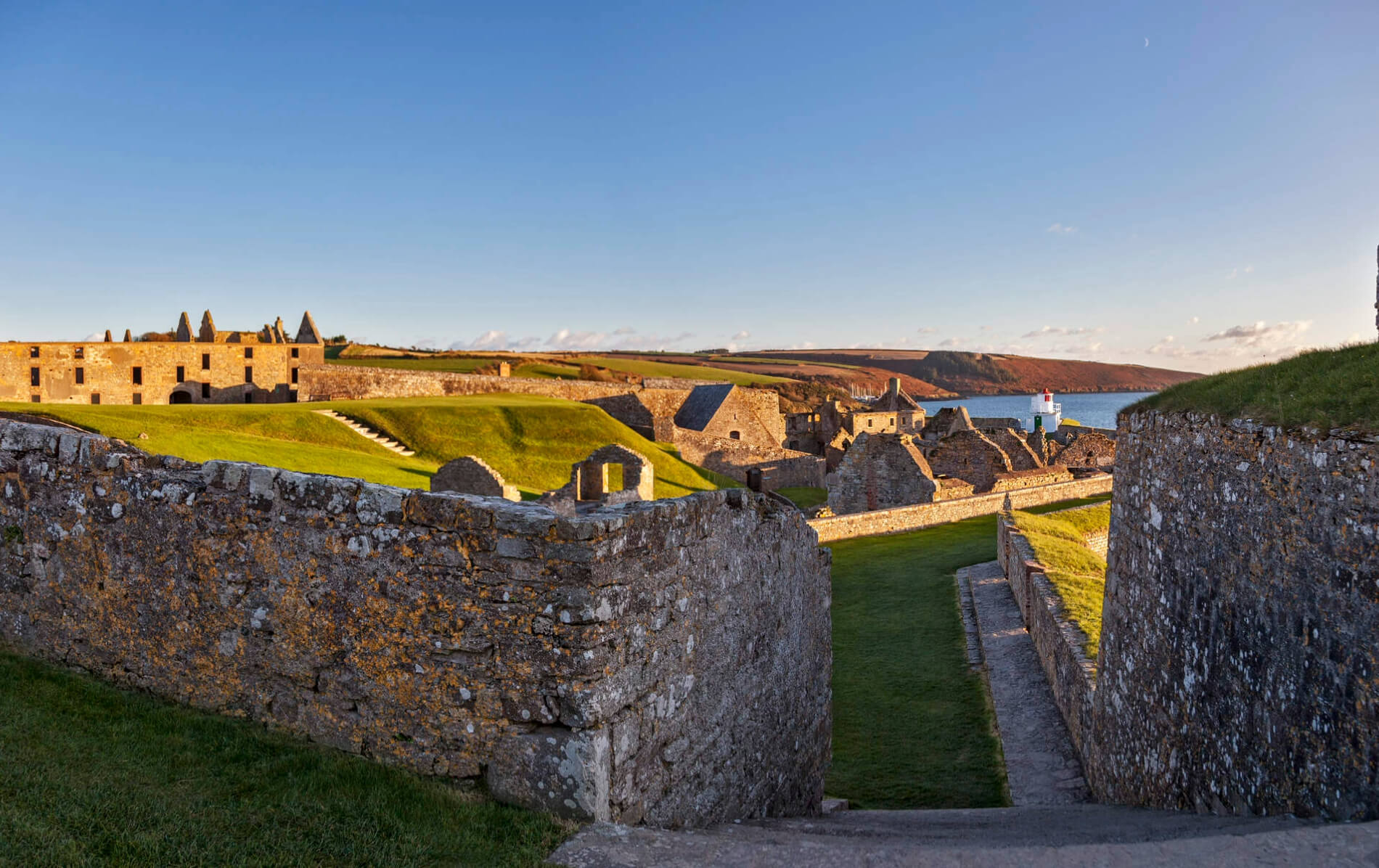 Stone walls and grassy ramparts of star-shaped Charles Fort overlook Kinsale Harbour under golden evening light.
