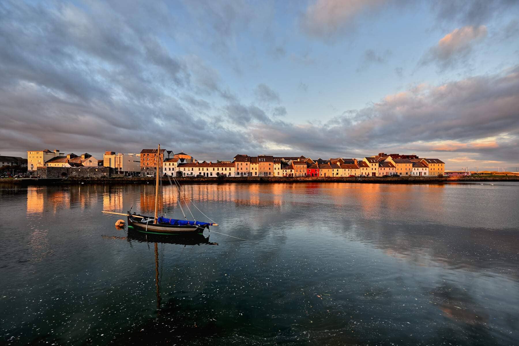 Reflections of colourful houses and a boat on calm evening water.