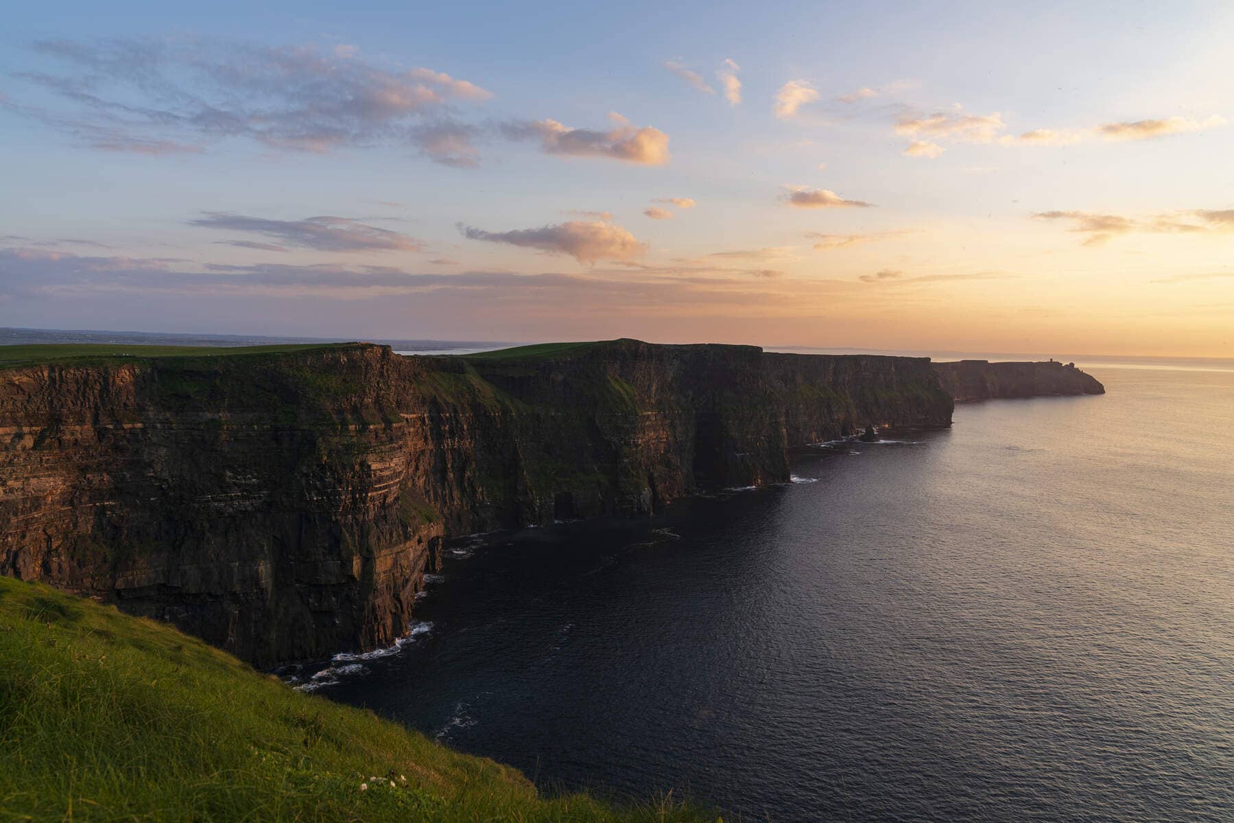 Towering sea cliffs stretch along the Atlantic coast, with the soft golden light of sunset reflecting off the water.