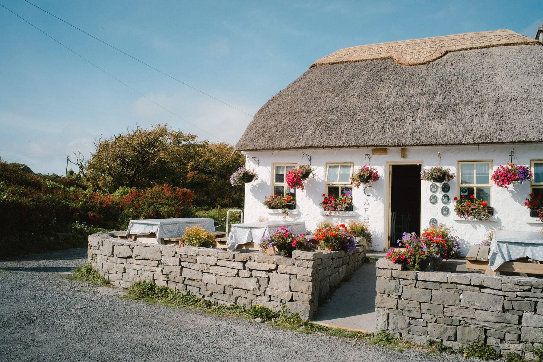 Restaurant in traditional Irish thatched cottage with blooming hanging baskets and outdoor seating.