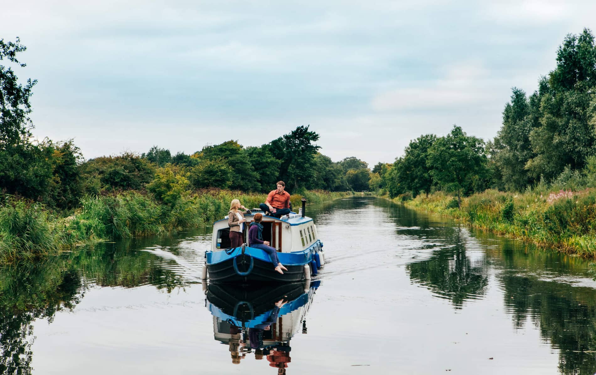 Family on a blue canal boat cruising through the Grand Canal in Sallins, County Kildare, surrounded by greenery.