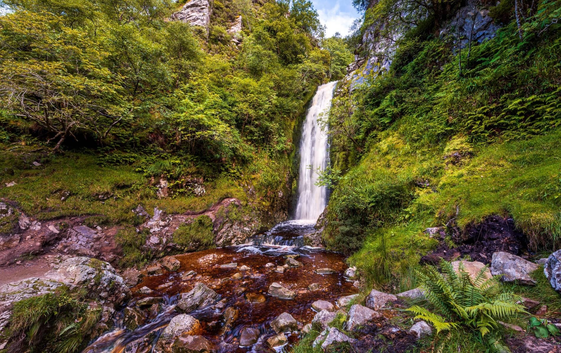 Una pintoresca cascada cae en una piscina rocosa rodeada de exuberante follaje verde en Glenevin, Donegal.