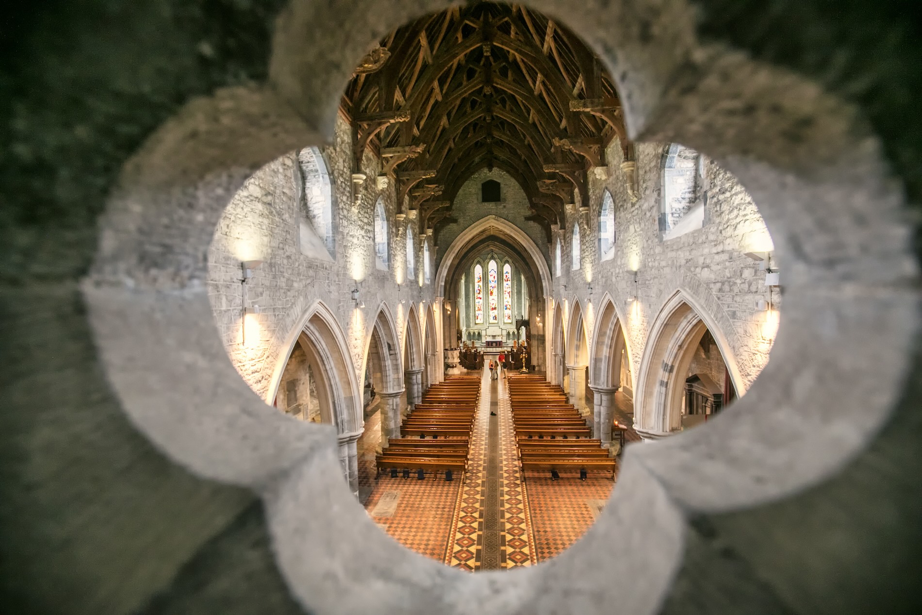 Interior of St Canice’s Cathedral viewed through a quatrefoil stone window, with ornate wooden roof.