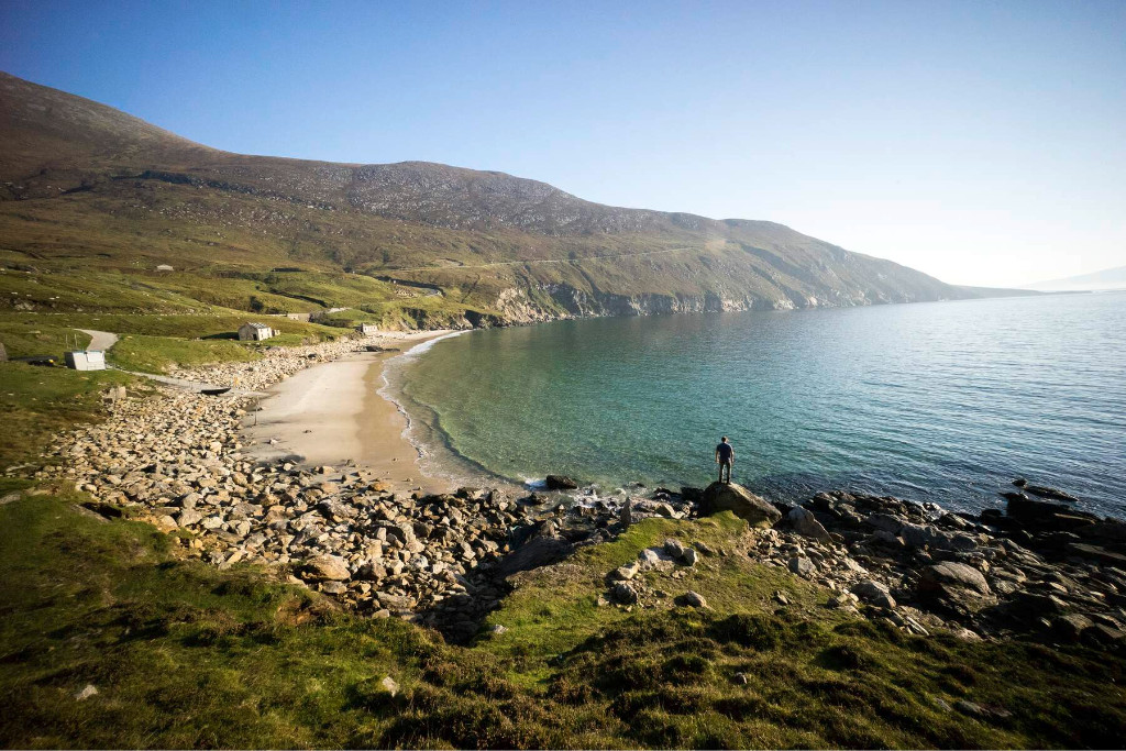 A secluded sandy beach in Keem Bay, framed by grassy hills and clear turquoise water.