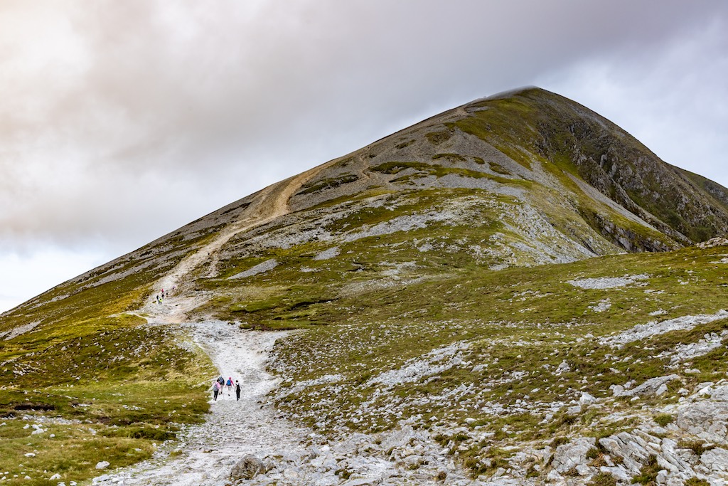 Hikers walking the rocky path up Croagh Patrick beneath grey skies and a steep slope.