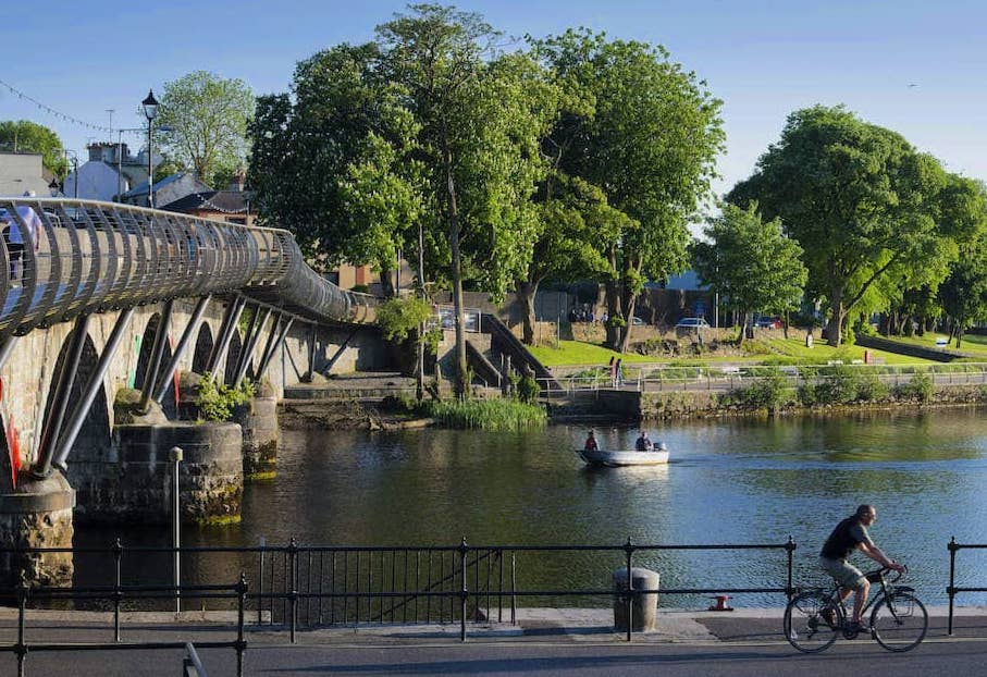 Cyclist and small boat on the River Shannon, near the footbridge in Carrick-on-Shannon on a sunny day.