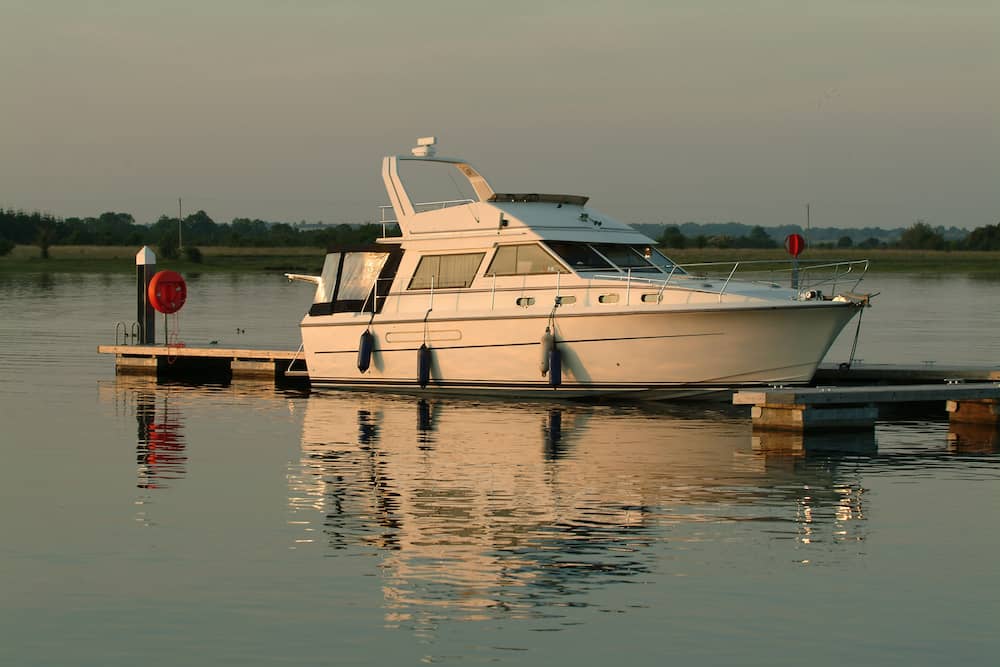 A white cruiser moored at a wooden jetty on the calm River Shannon during golden evening light.
