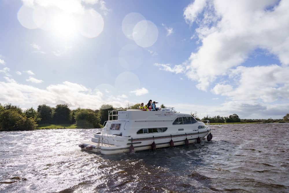 Cruiser boat on the River Shannon at Banagher with families on deck and sun breaking through clouds