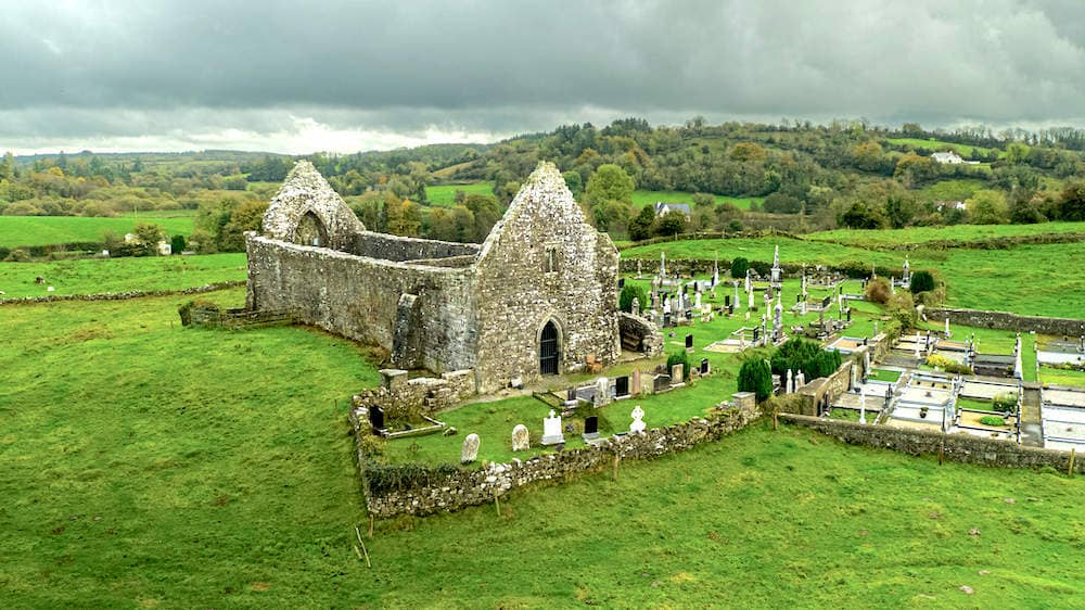 Ruins of medieval Jamestown Abbey and gravestones nestled in green fields under overcast skies.